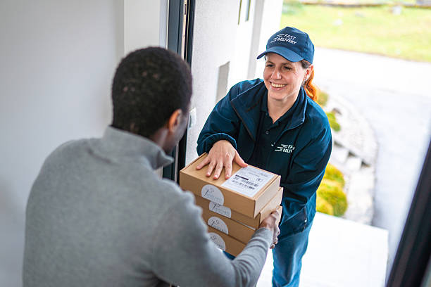 笑顔の配達員が男性の受取人に荷物を手渡す - door-to-door international shipping ストックフォトと画像